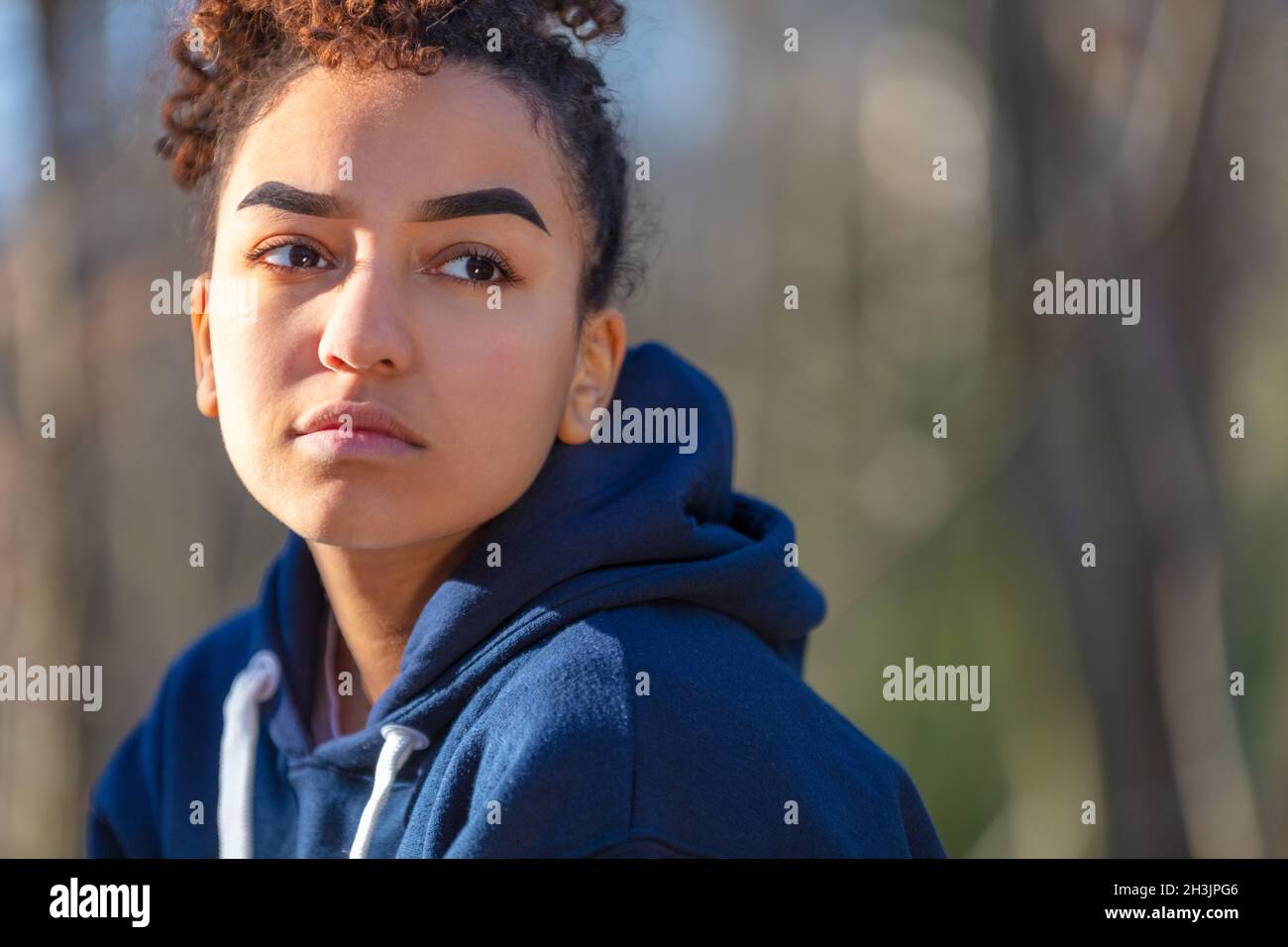 Outdoor portrait of sad depressed or thoughtful mixed race biracial African American girl teenager female young woman wearing a blue hoodie Stock Photo