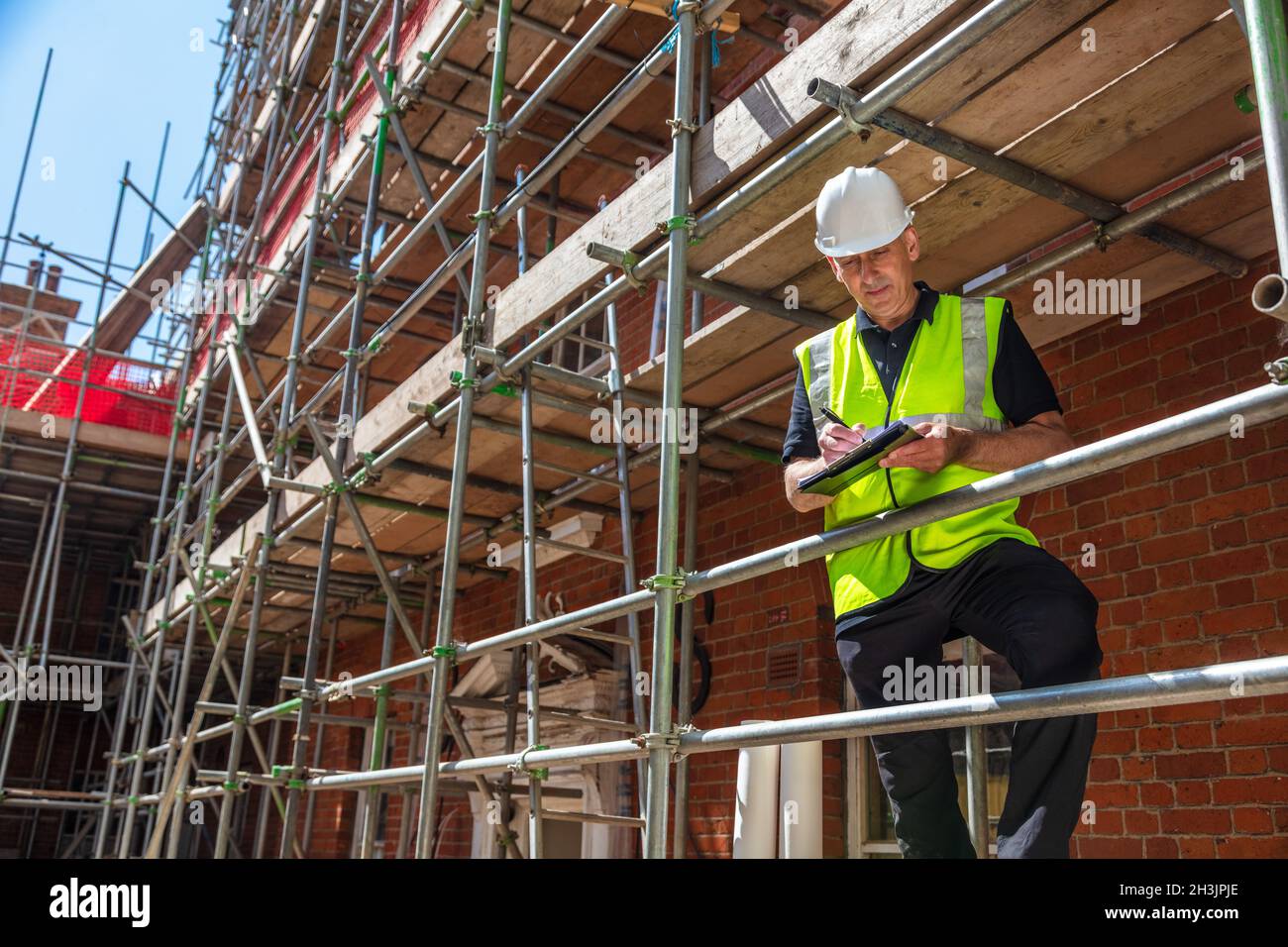 Male builder foreman, construction worker, contractor or architect on building site writing on black clipboard Stock Photo