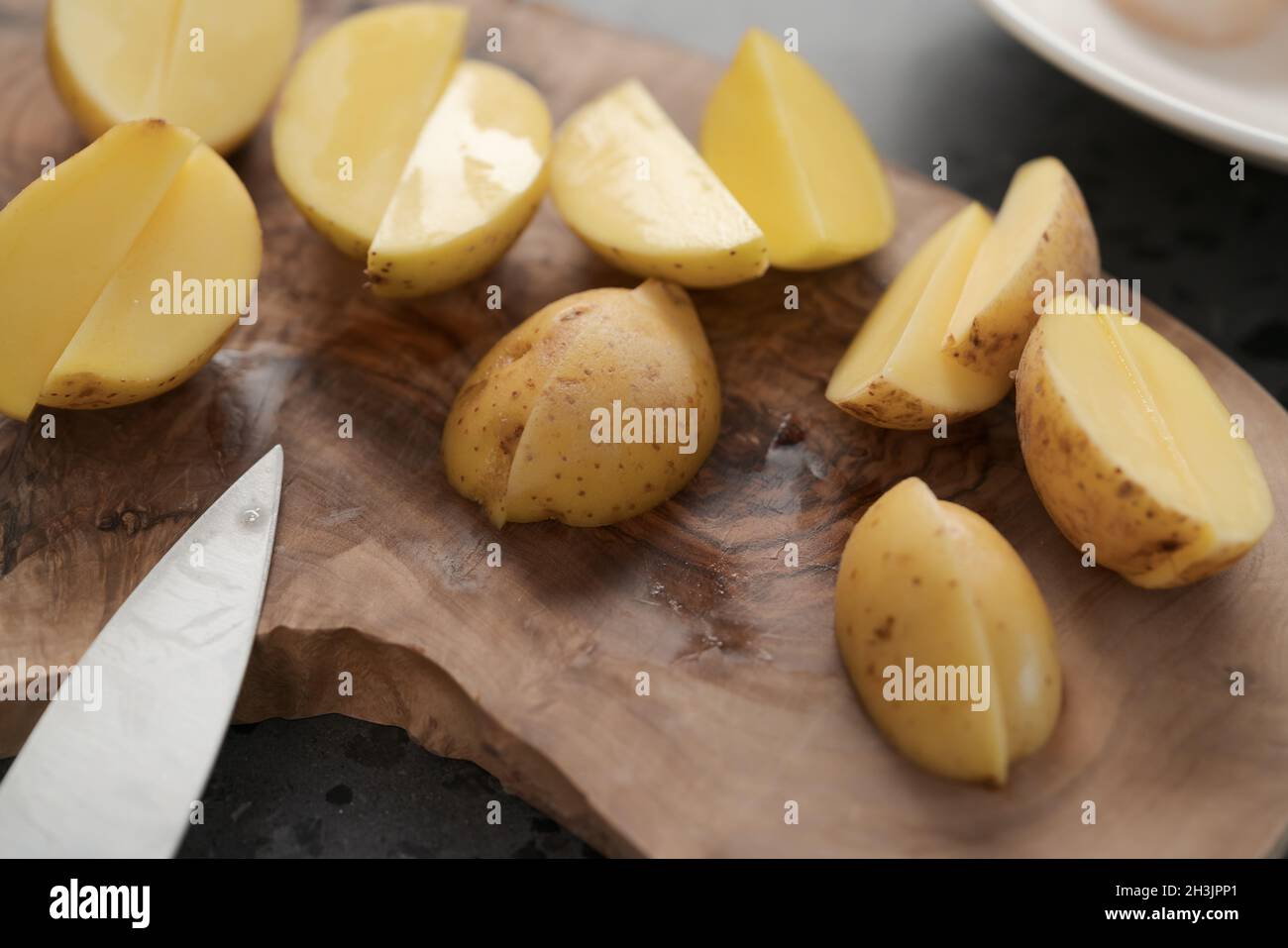 Raw washed and chopped baby potatoes ready to cook on olive wood board, shallow focus Stock Photo