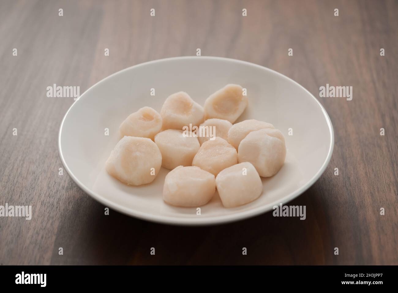 frozen scallops in white bowl on walnut table for defrosting, shallow focus Stock Photo