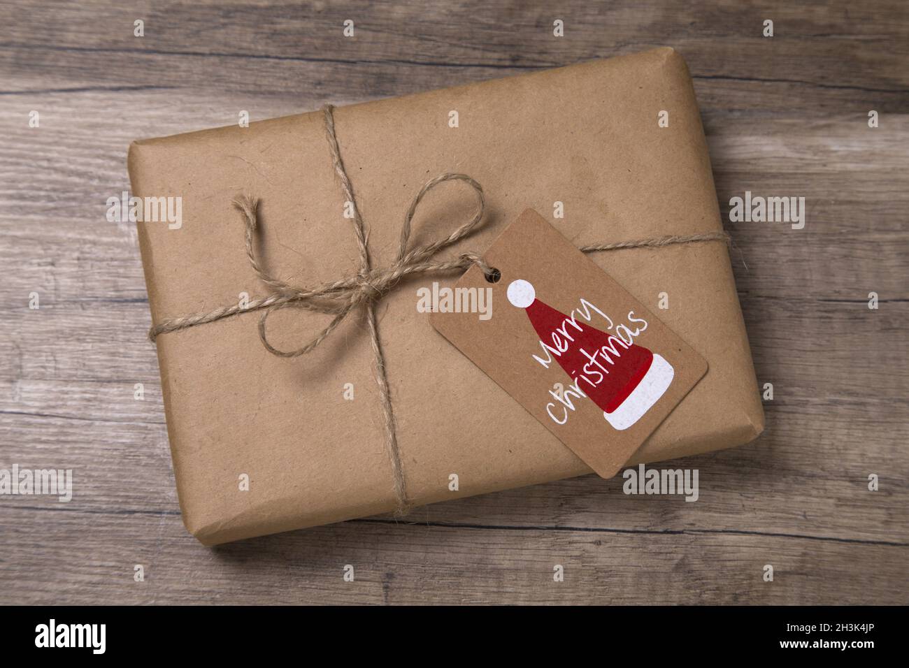 Christmas or New Year gift box wrapped in kraft paper with blank gift tag on old wooden background. Stock Photo