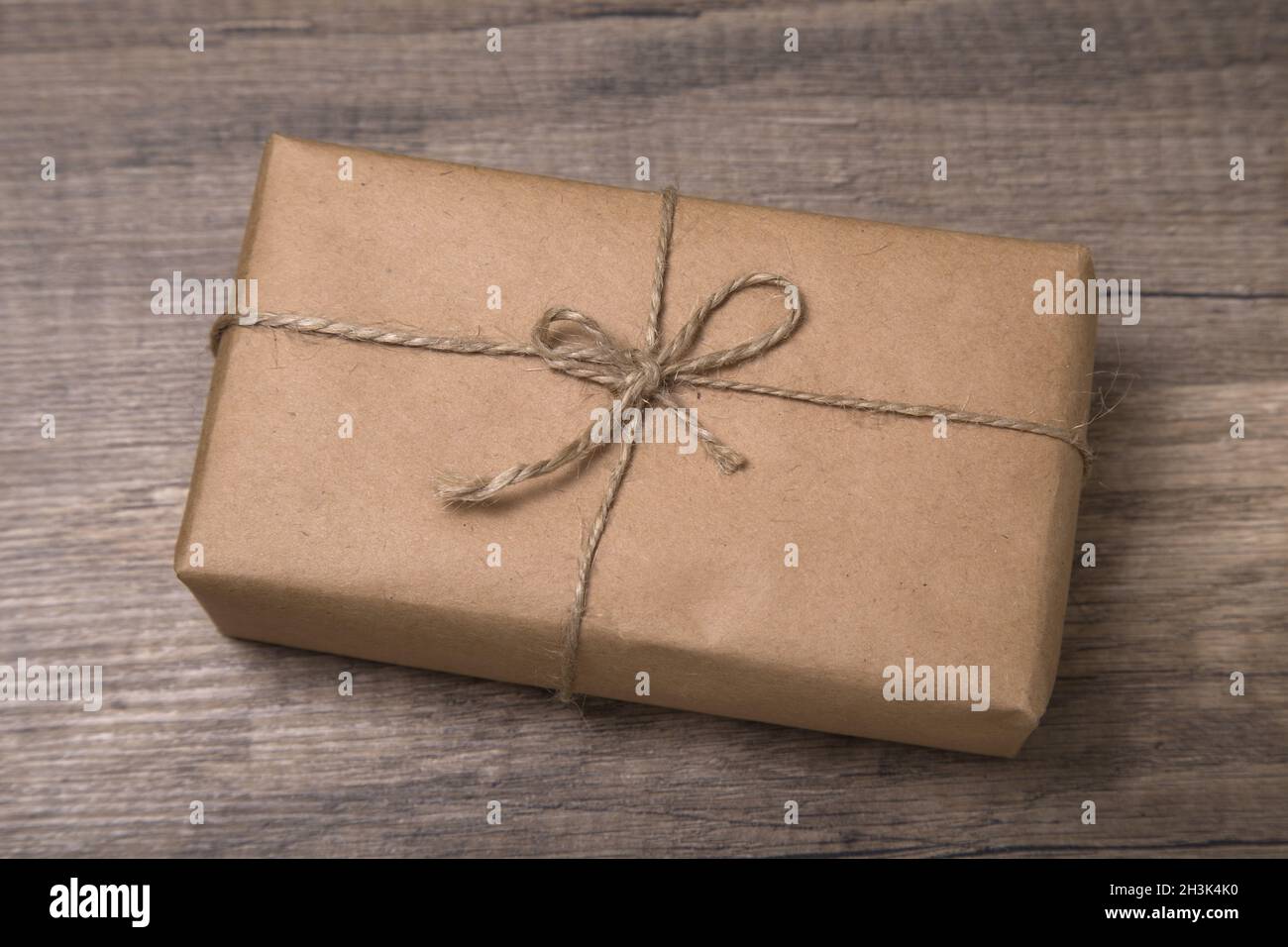 Christmas or New Year gift box wrapped in kraft paper with blank gift tag on old wooden background. Stock Photo