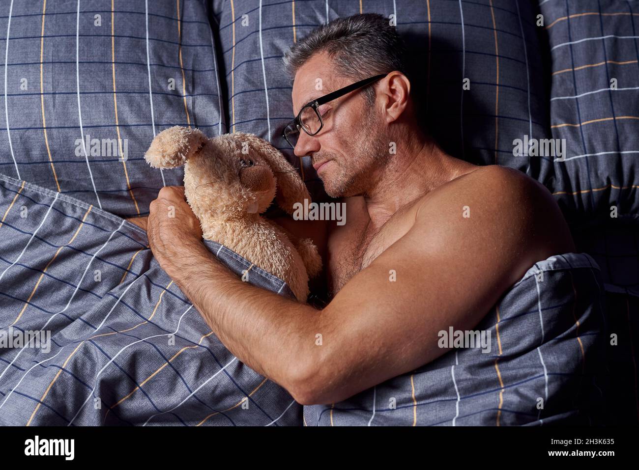 A young man sleeps in an embrace with a stuffed rabbit in bed. Stock Photo