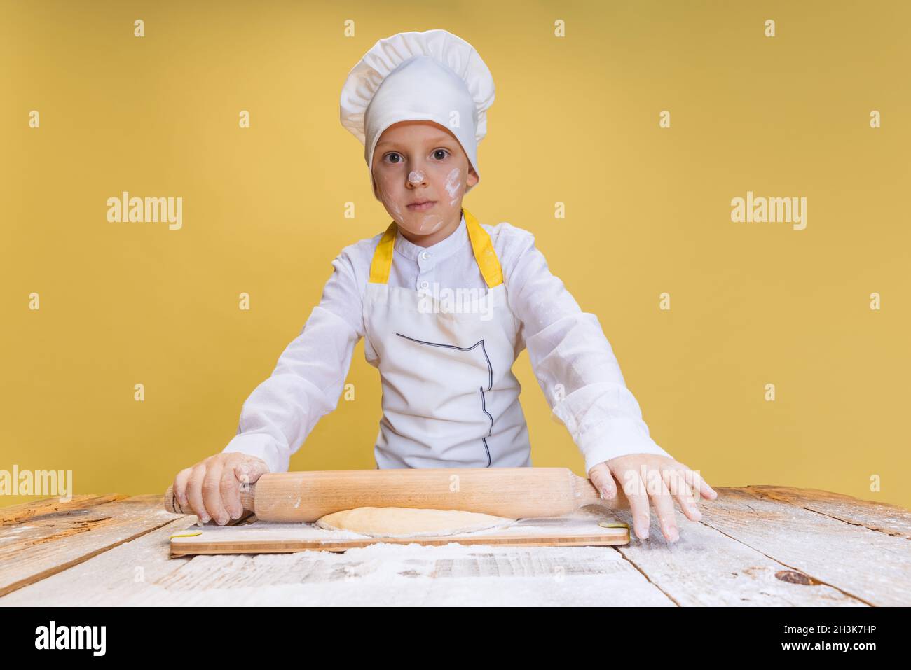 One cute boy wearing in white cook chef jacket and hat kneads dough isolated on yellow studio background Stock Photo Alamy