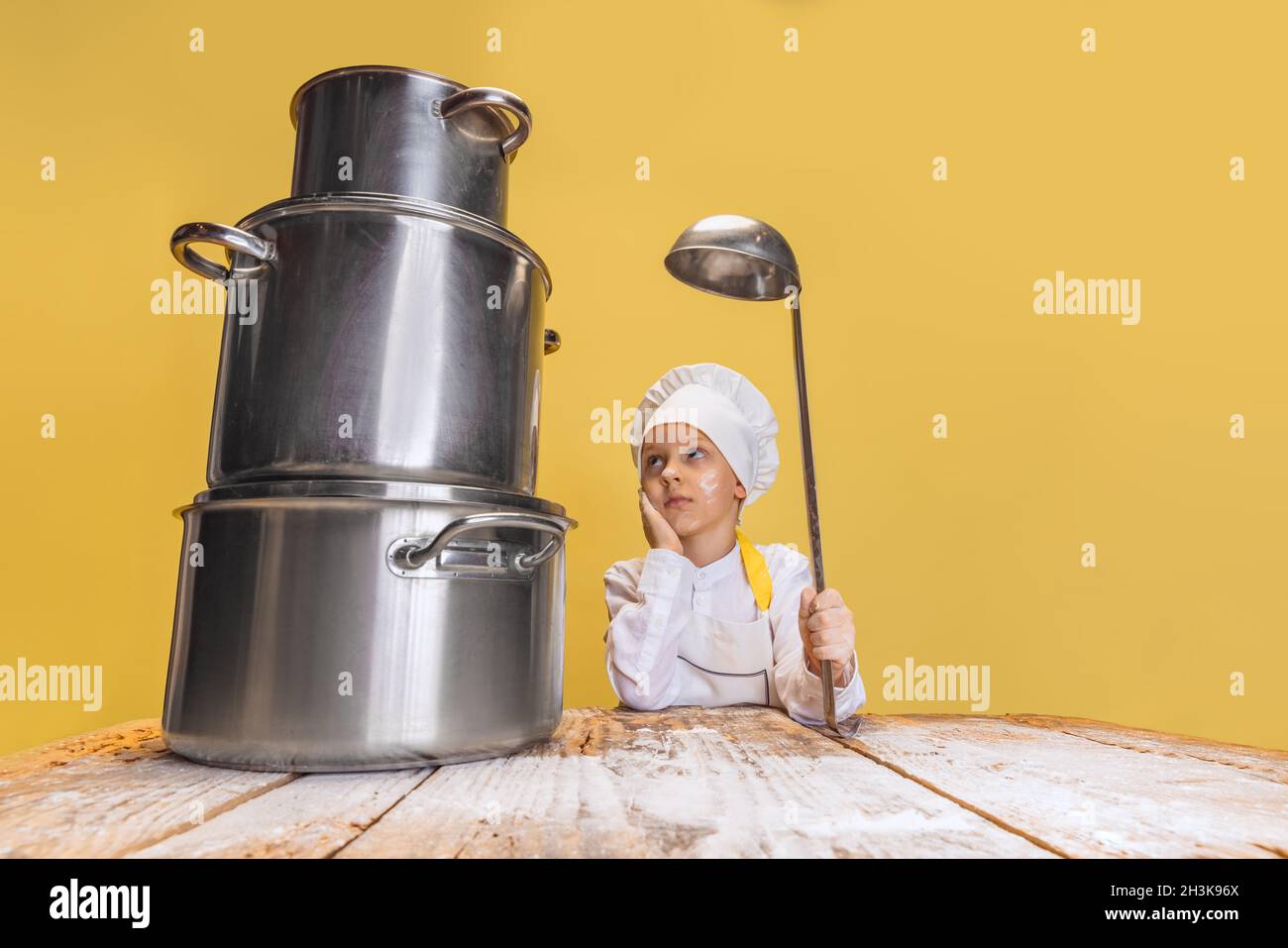 https://c8.alamy.com/comp/2H3K96X/close-up-cute-little-boy-in-white-cook-uniform-and-huge-chefs-hat-at-kids-kitchen-with-big-pans-isolated-on-yellow-studio-background-2H3K96X.jpg