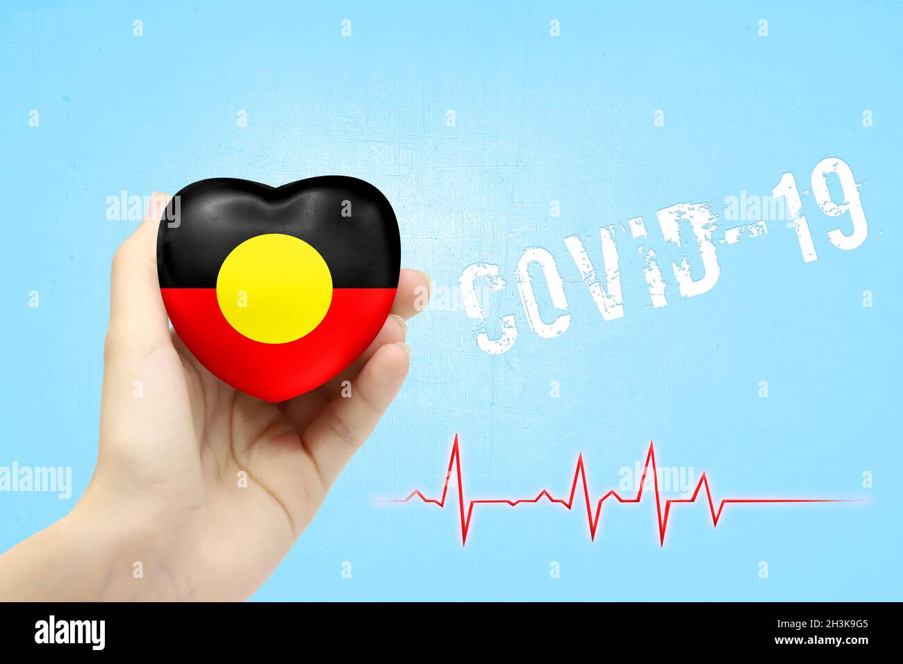 A girl is holding a toy in the shape of a heart with the flag of Australian Aboriginal, a concept of health care during the covid-19 coronavirus pande Stock Photo