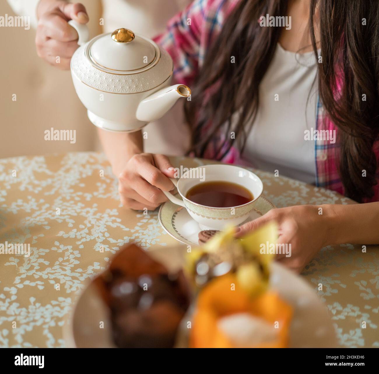 Pouring tea from porcelain teapot to the cup. Stock Photo