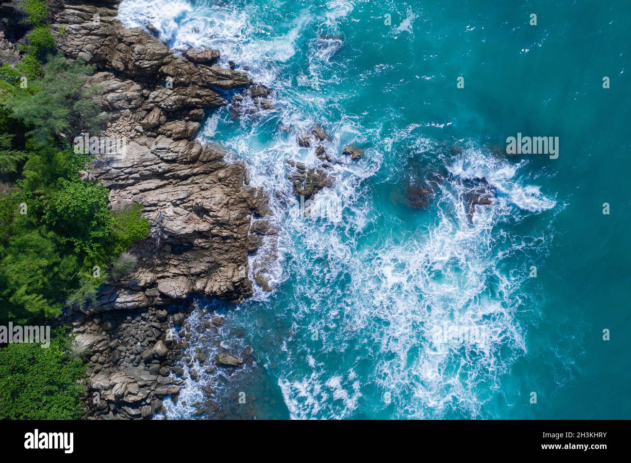 Aerial top view of ocean's beautiful waves crashing on the rocky island coast Stock Photo