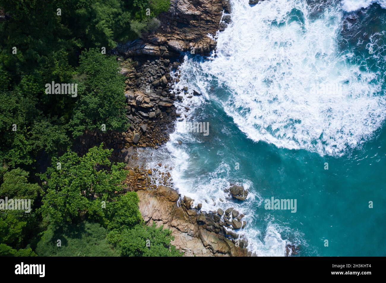 Aerial top view of ocean's beautiful waves and rocky coast with greenery Stock Photo