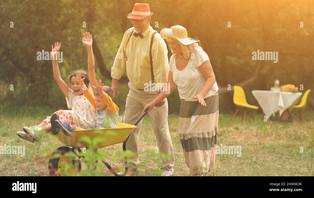 Grandma and grandpa are pushing their grandchildren in a wheelbarrow Stock Photo