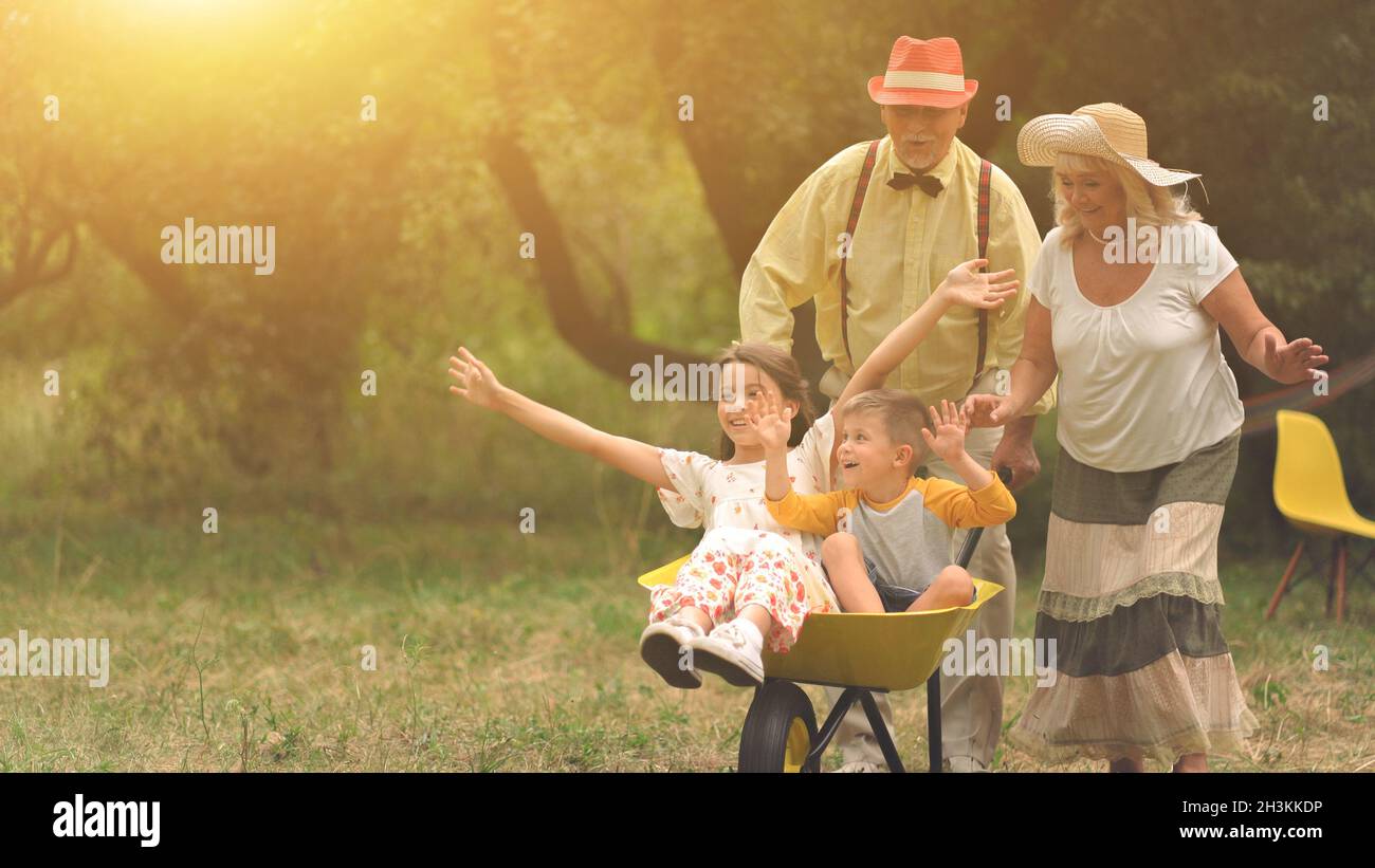 Grandma and grandpa are pushing their grandchildren in a wheelbarrow2 Stock Photo