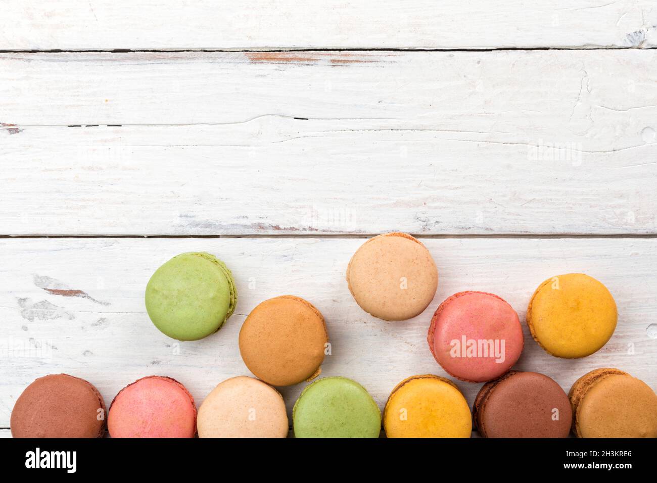 Border of colorful macarons pastry on rustic table high angle view. Flat lay pastel colored French gourmet candy assortment greeting card with copy sp Stock Photo