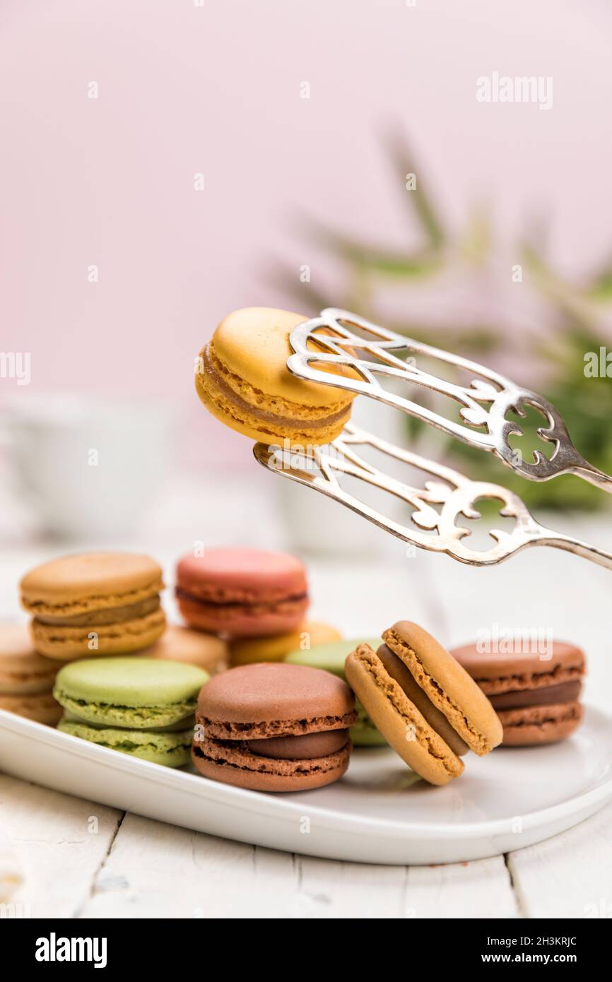 Assortment of French macarons pastry on coffee table, a lemon flavored one held up with pastry tongs Stock Photo