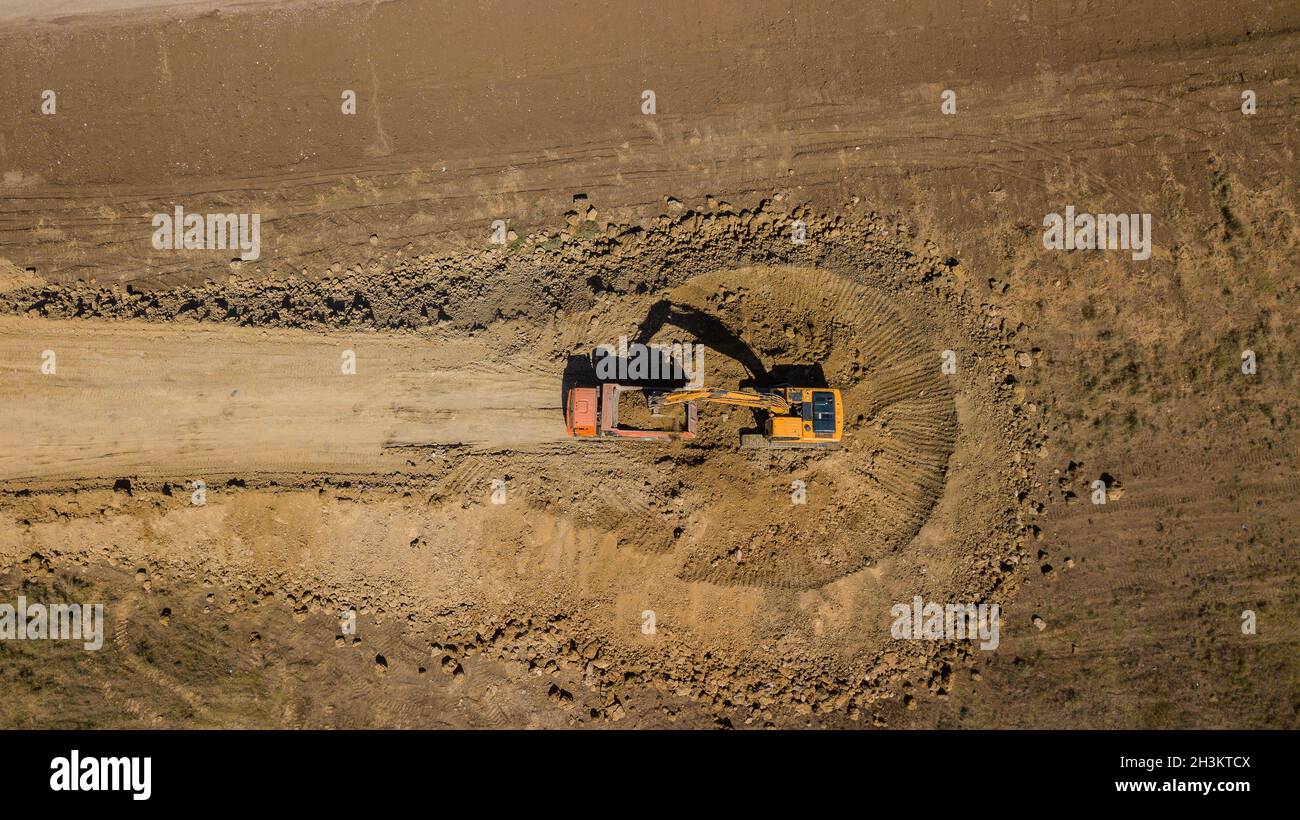 Aerial shot of excavator pours sand into the truck. On the construction site top view. Shooting from the drone. Stock Photo