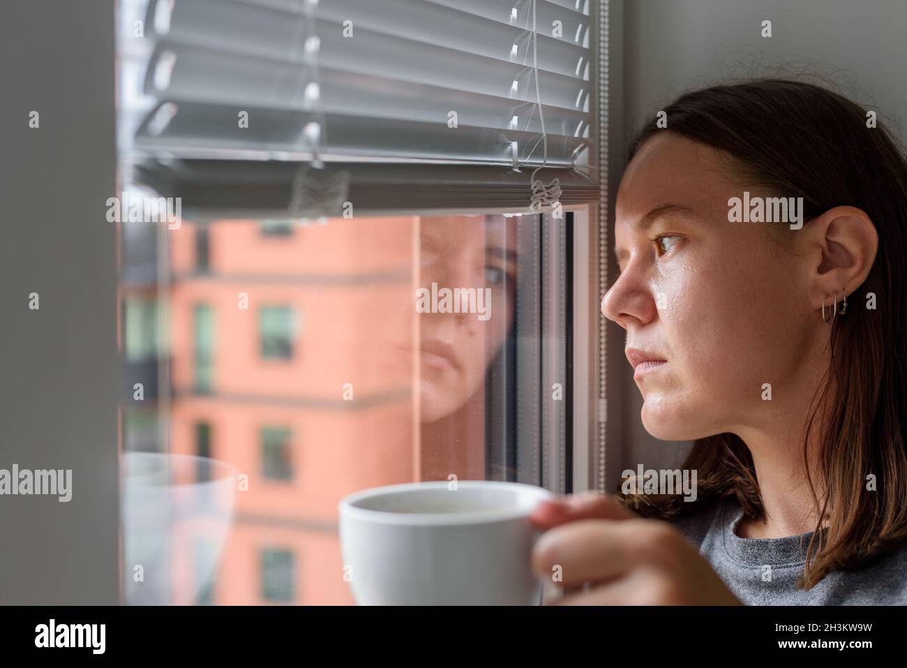 Anxious woman with cup looking to window and waiting Stock Photo