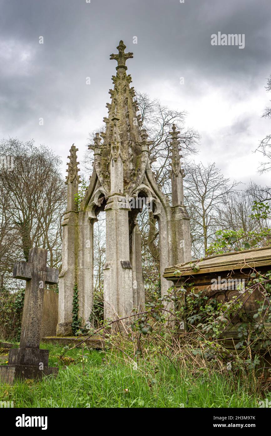 An old gothic tomb tomb in an overgrown graveyard on a dull cloudy day. Stock Photo