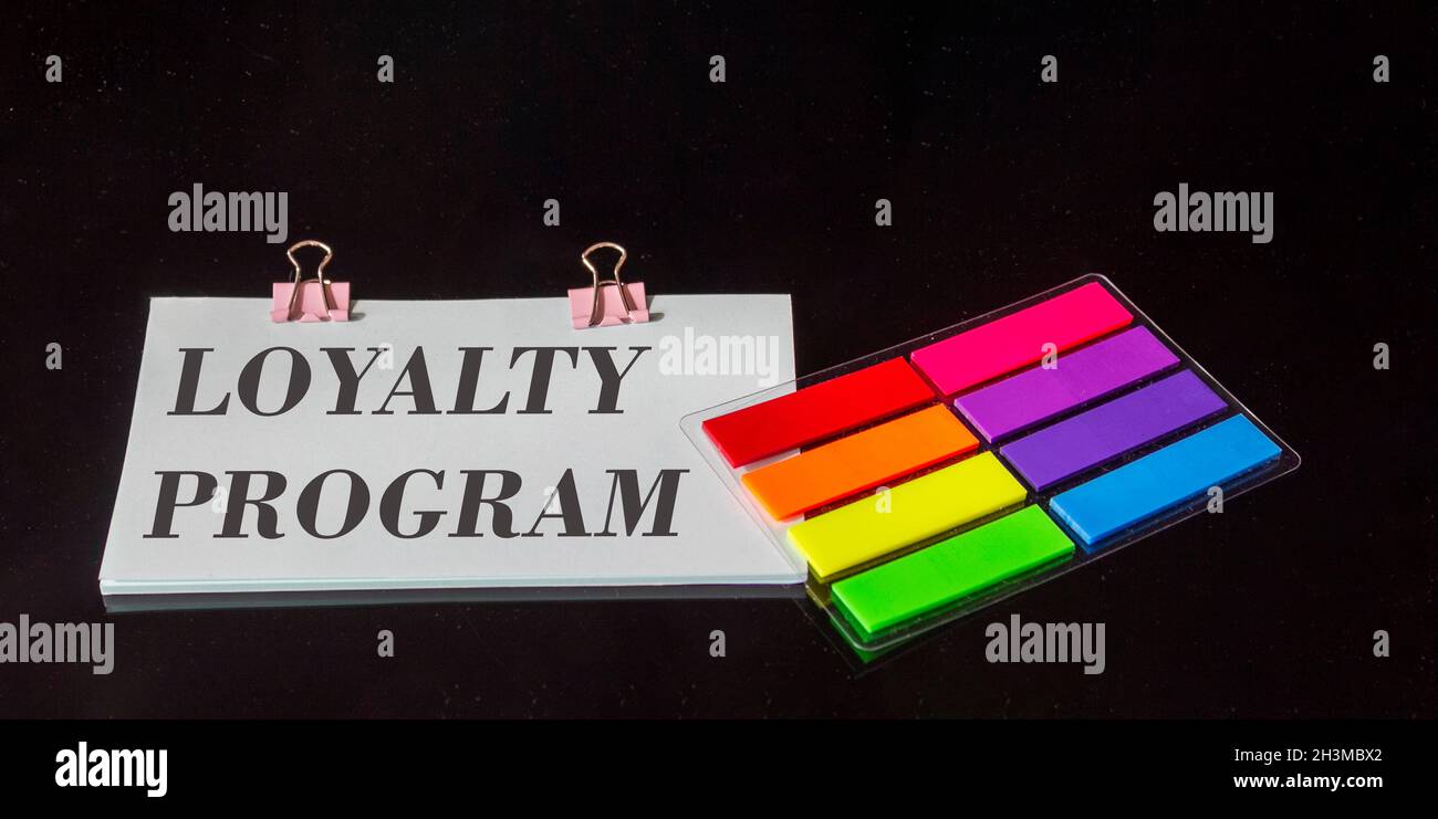 The text Loyalty program is written on a sticker, next to the colored stickers on a black glass background Stock Photo