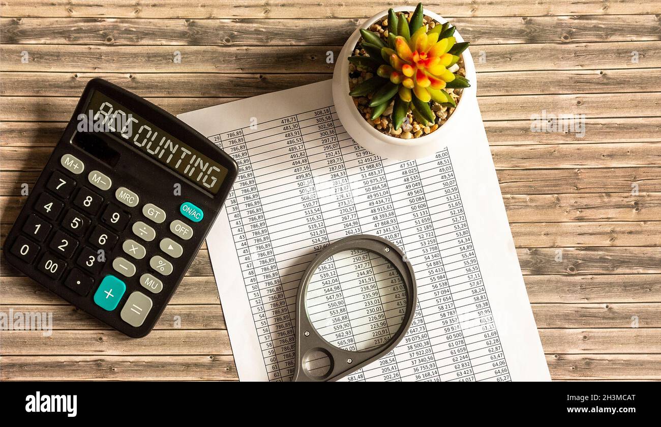 Accounting, the text is written on a calculator, bills, a magnifying glass  and a pot of flowers lie on a wooden table Stock Photo - Alamy