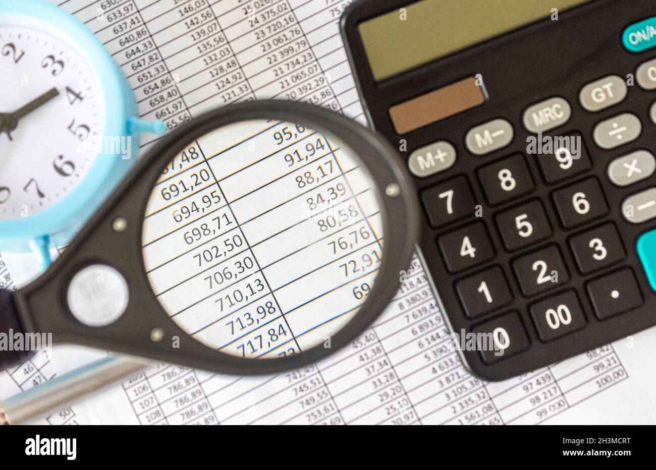 A magnifying glass examines the numbers in a document, next to a calculator,  a clock and a pen Stock Photo - Alamy