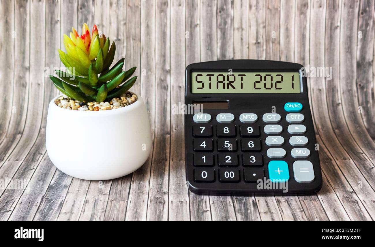 On the calculator, the text START 2021, next to a cactus flower on a wooden table. Planning, business, motivation and inspiration concept Stock Photo