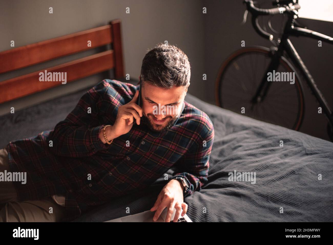 Happy man talking on smart phone while using laptop computer at home Stock Photo