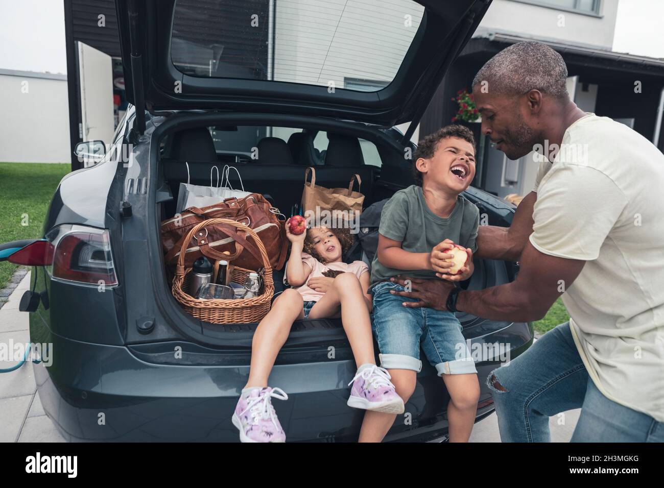 Father tickling son sitting by girl in car trunk at front yard Stock Photo