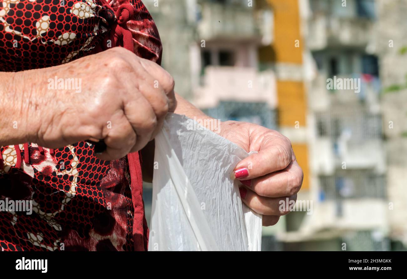 Close up of senior Caucasian female hands with senile spots on her skin. She is holding a nylon small bag. Her nails are not done. Stock Photo