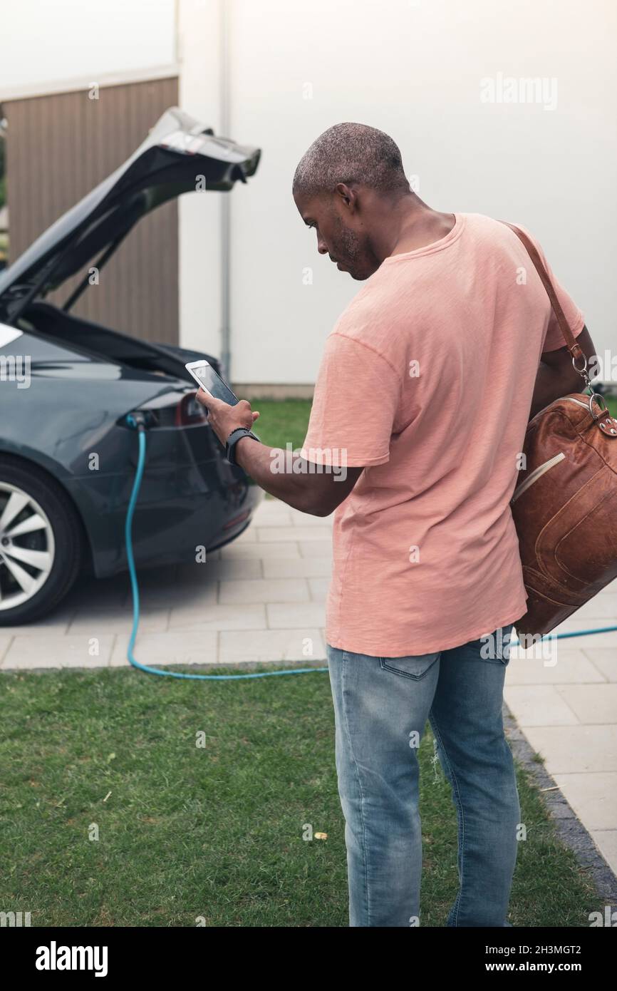 Rear view of man using smart phone while standing with backpack at charging station Stock Photo