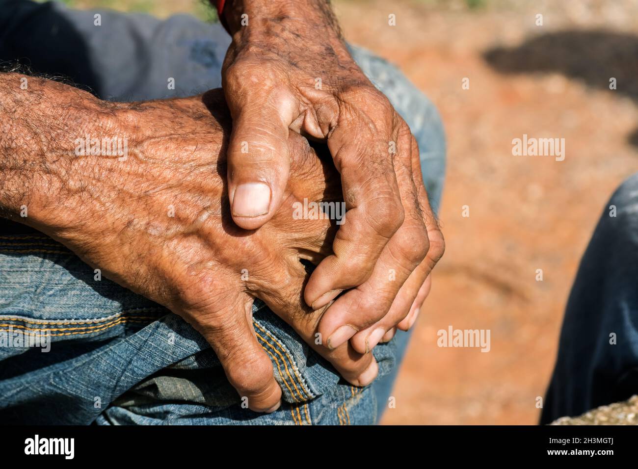 Close up of both hands of a dark skin senior man, one hand is on top of the other, hands on his knee. Stock Photo