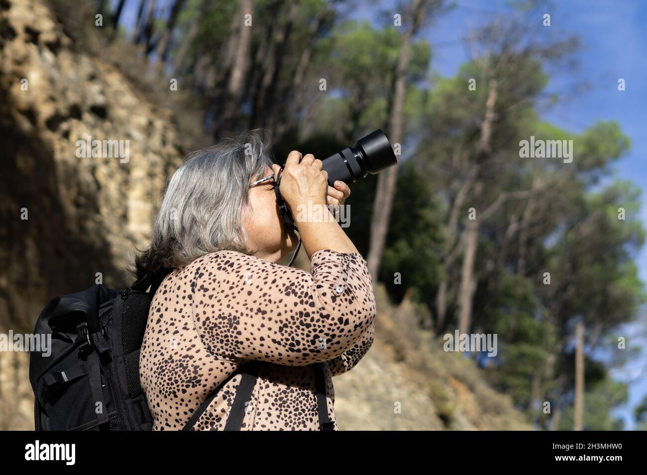 older white-haired woman taking pictures in the forest Stock Photo