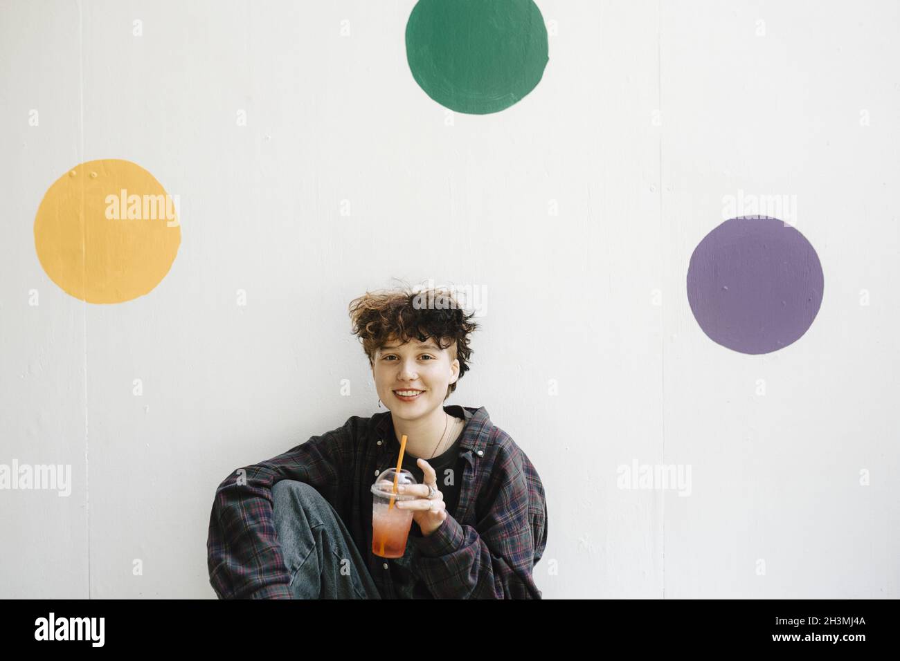 Portrait of smiling teenage boy drinking against polka dots on white wall Stock Photo