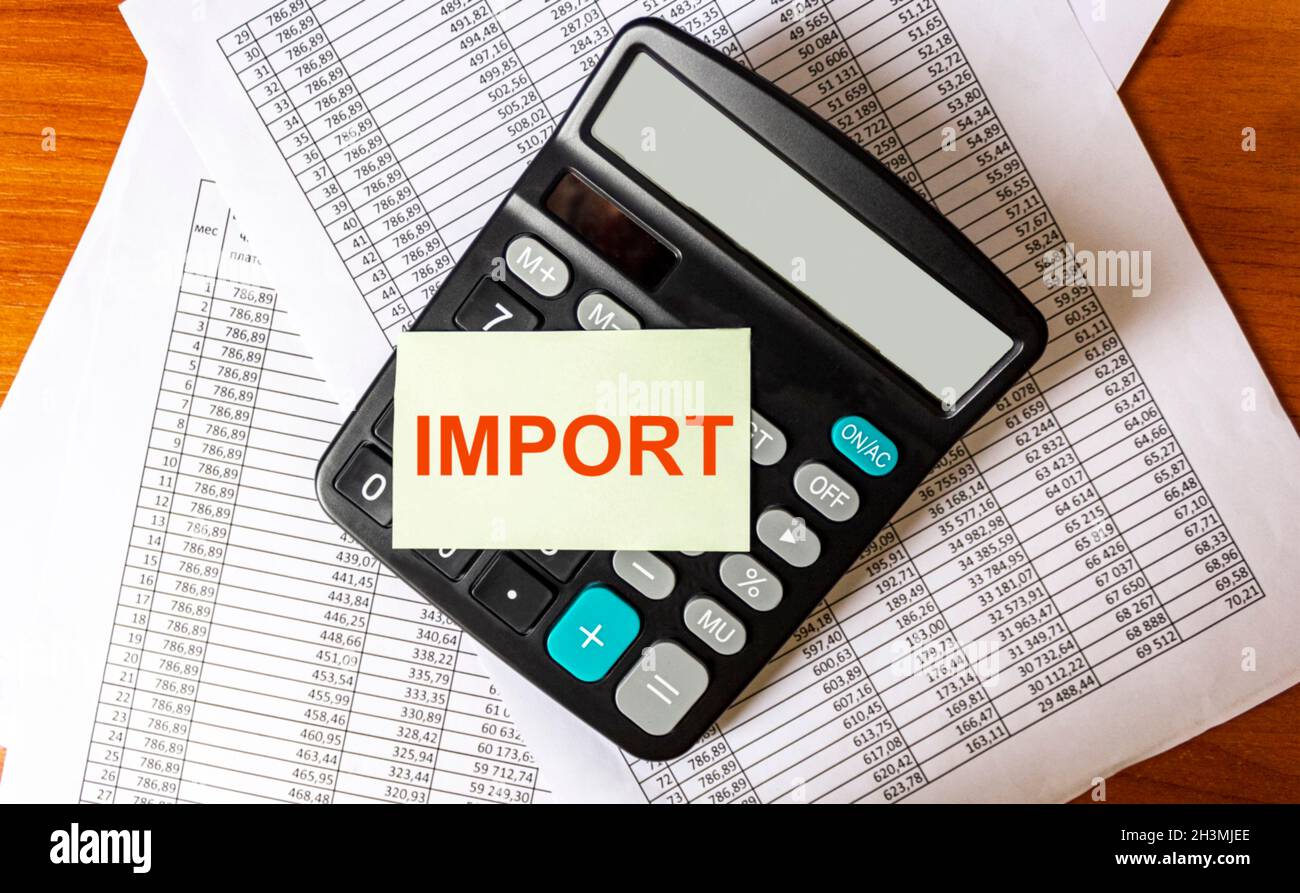 The word IMPORT on a white sticker on a calculator and papers on a wooden table. Stock Photo