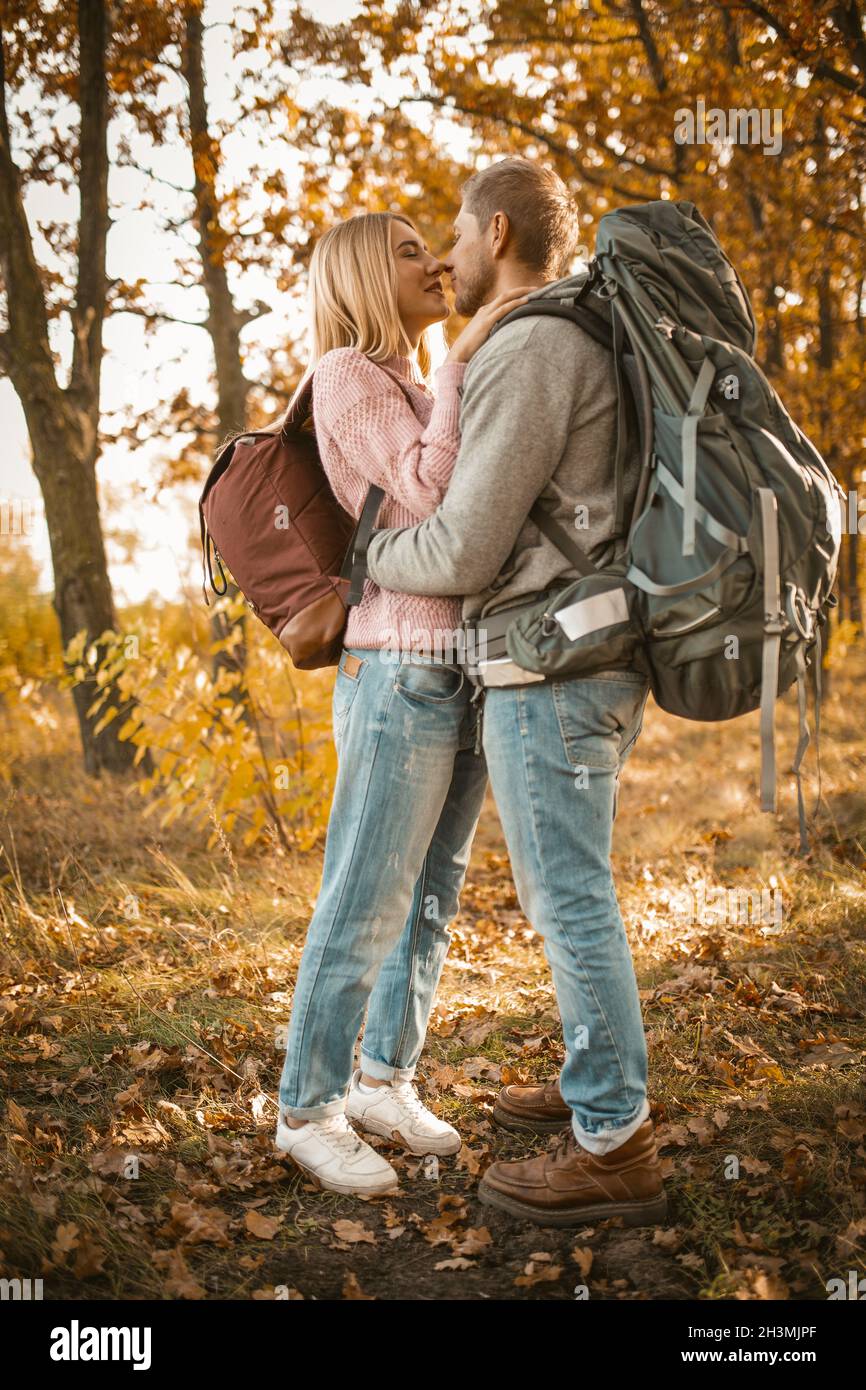 Couple of tourists in love in the autumn forest. Young man and woman kisses and hugs while standing against the backdrop of colo Stock Photo