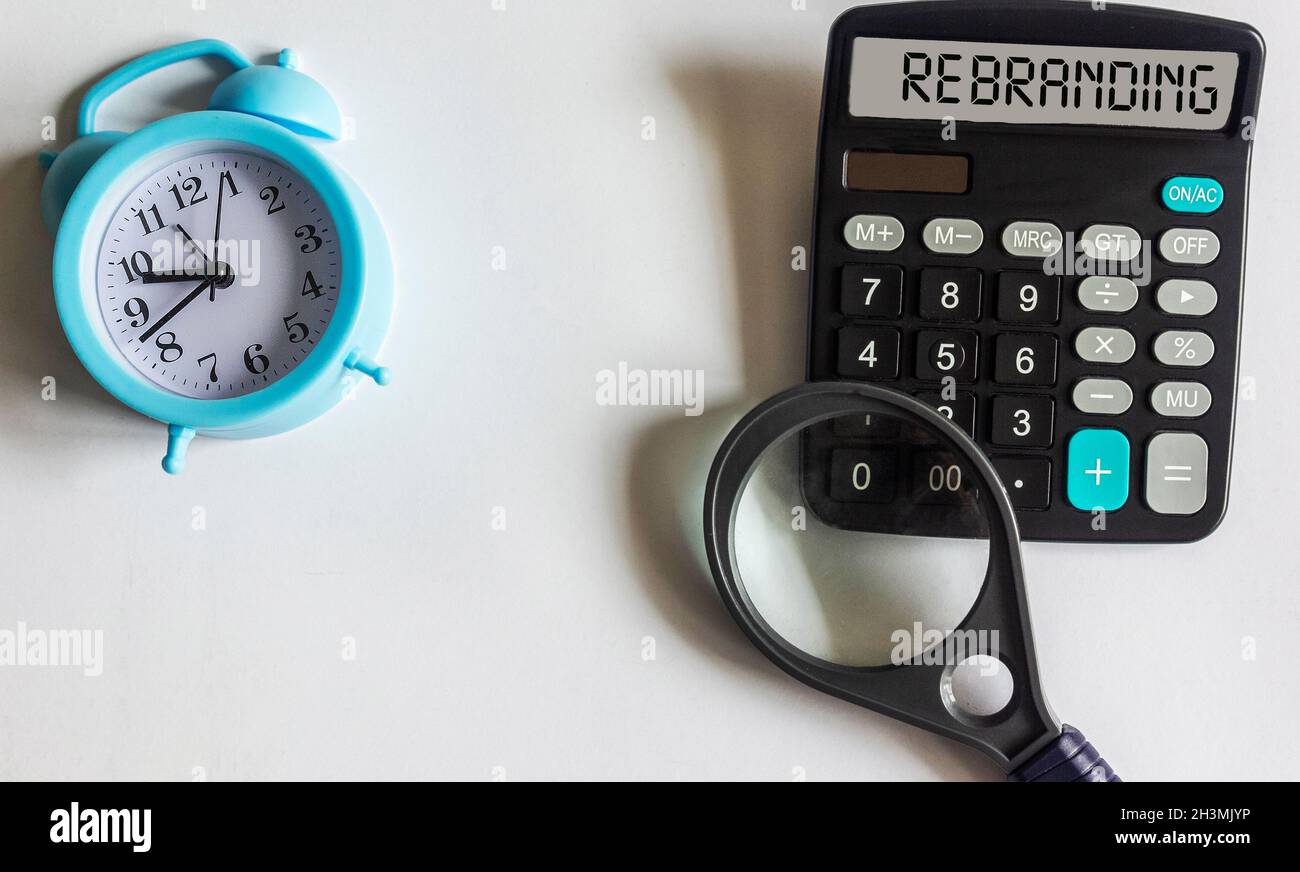 The display of the calculator text Rebranding, next to an alarm clock and a magnifying glass on a white background. Stock Photo