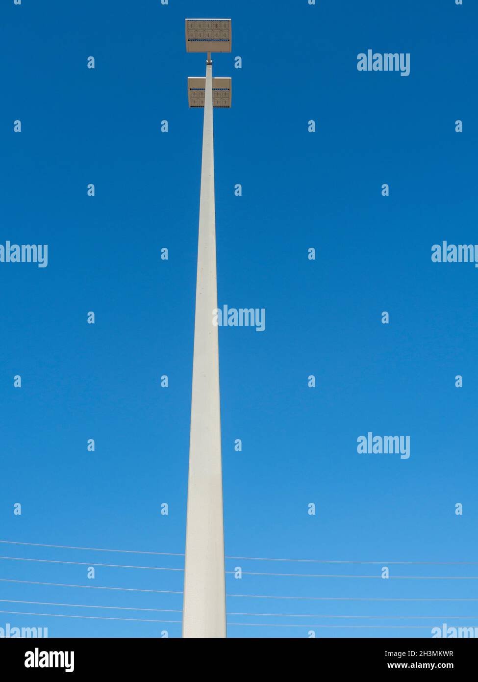 LED Parking Lot Lights: Two panels of high intensity LEDs extend high into a bright blue sky above a commercial parking lot. Stock Photo