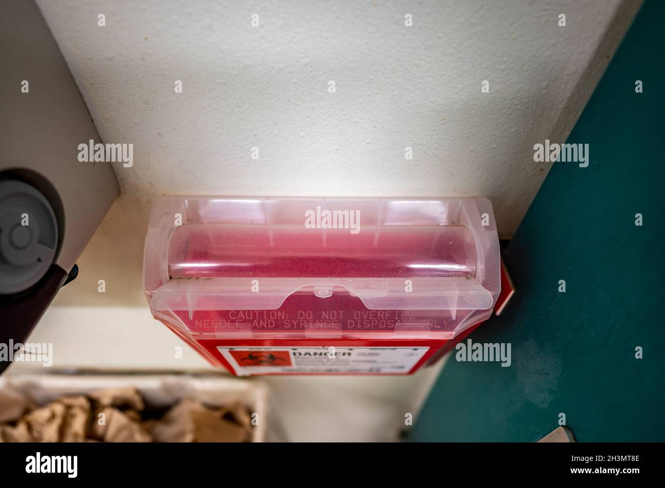 Red biohazard sharps waste container mounted to the wall of a public