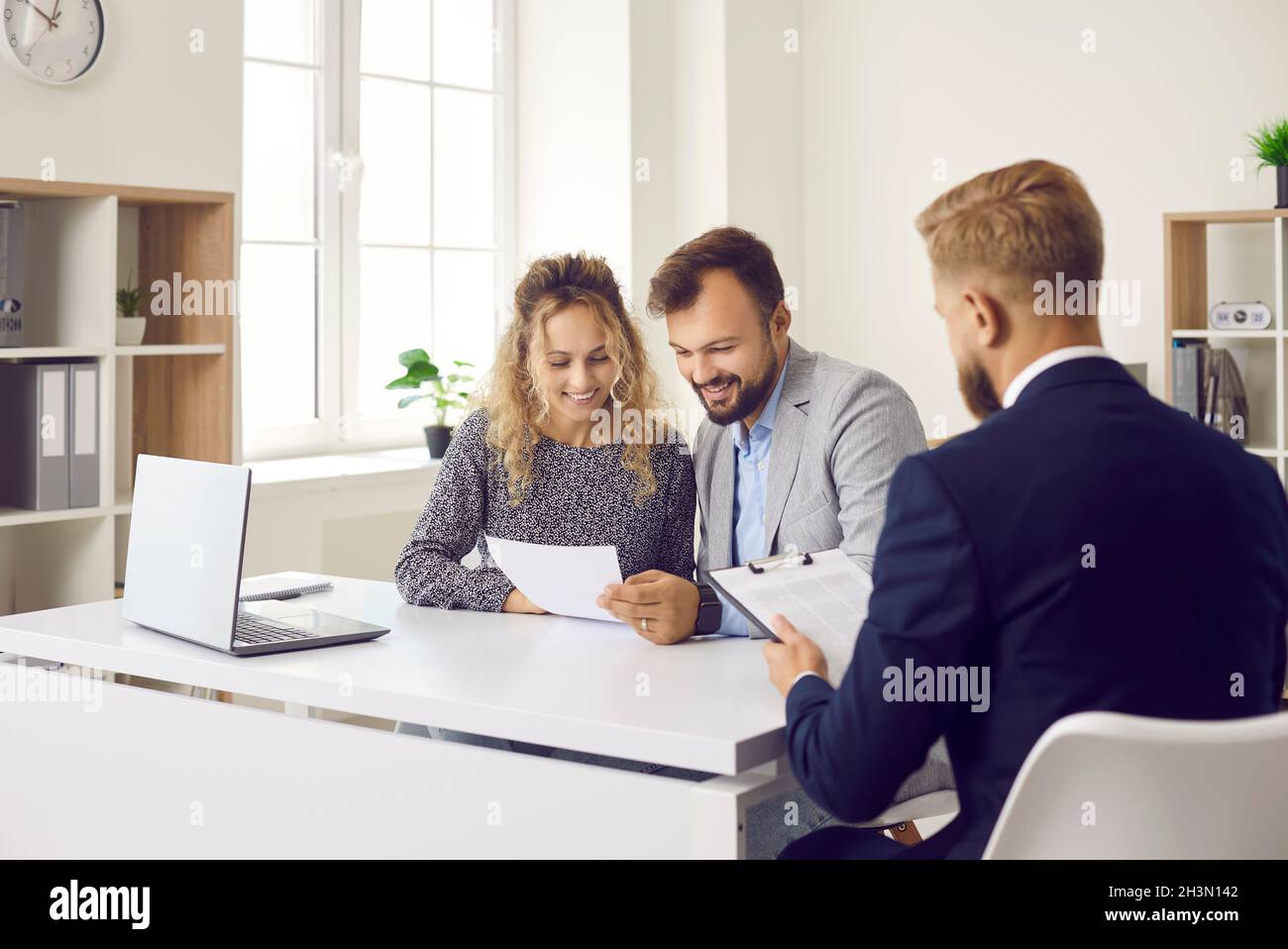 Clients sitting at desk in real estate agent's office and reading contract that he gave them Stock Photo