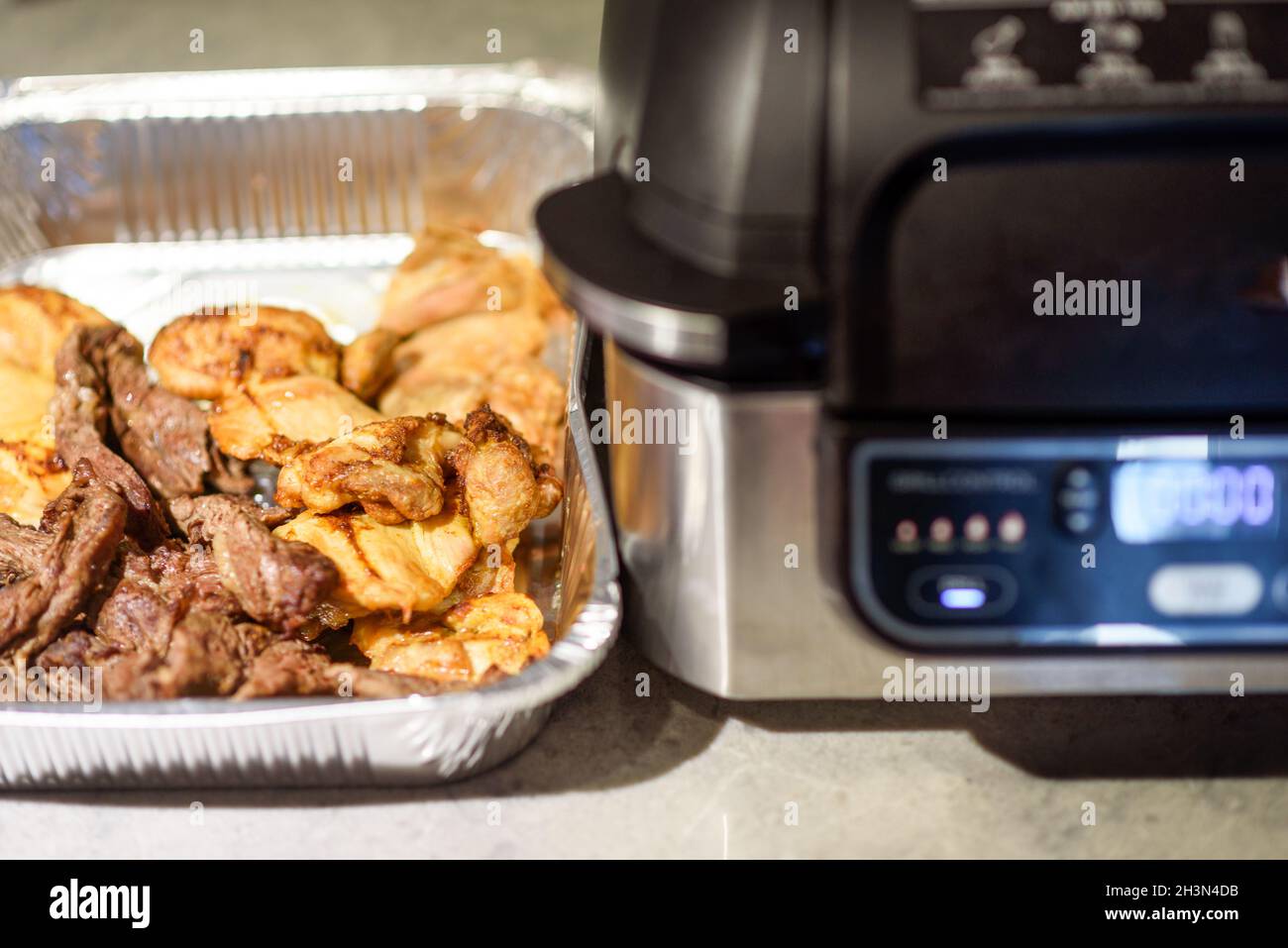 Air fryer in kitchen. Cooking meat with spices in an air fryer. Selective focus on meat in tray. Stock Photo