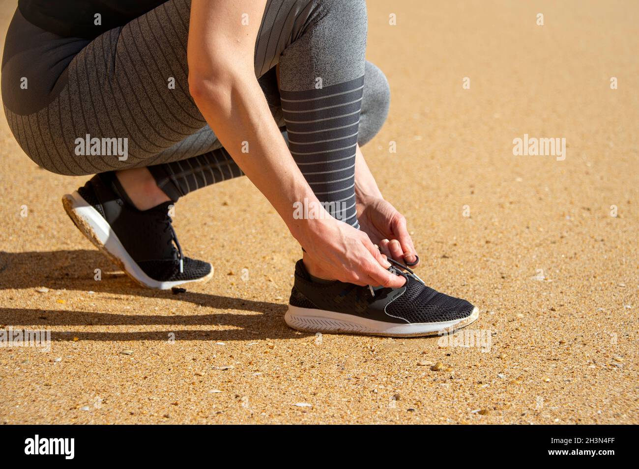 Close up of a sporty woman tying up her shoelaces on her running shoes on sand. Stock Photo