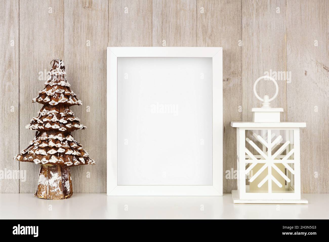Mock up white frame with Christmas tree and lantern decor on a shelf