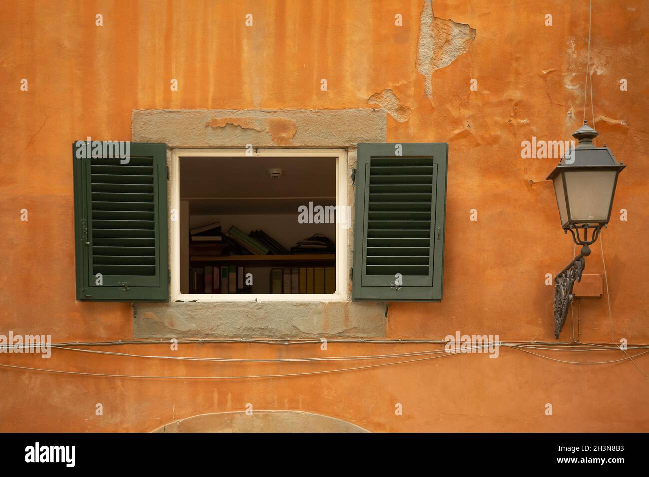 Opened window with green shutters on orange wall of old building Stock Photo