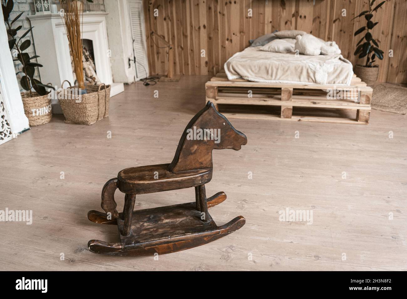 Bedroom in the interior of wood with a wooden horse. There's a children's horse in the foreground. In the background is a bed an Stock Photo