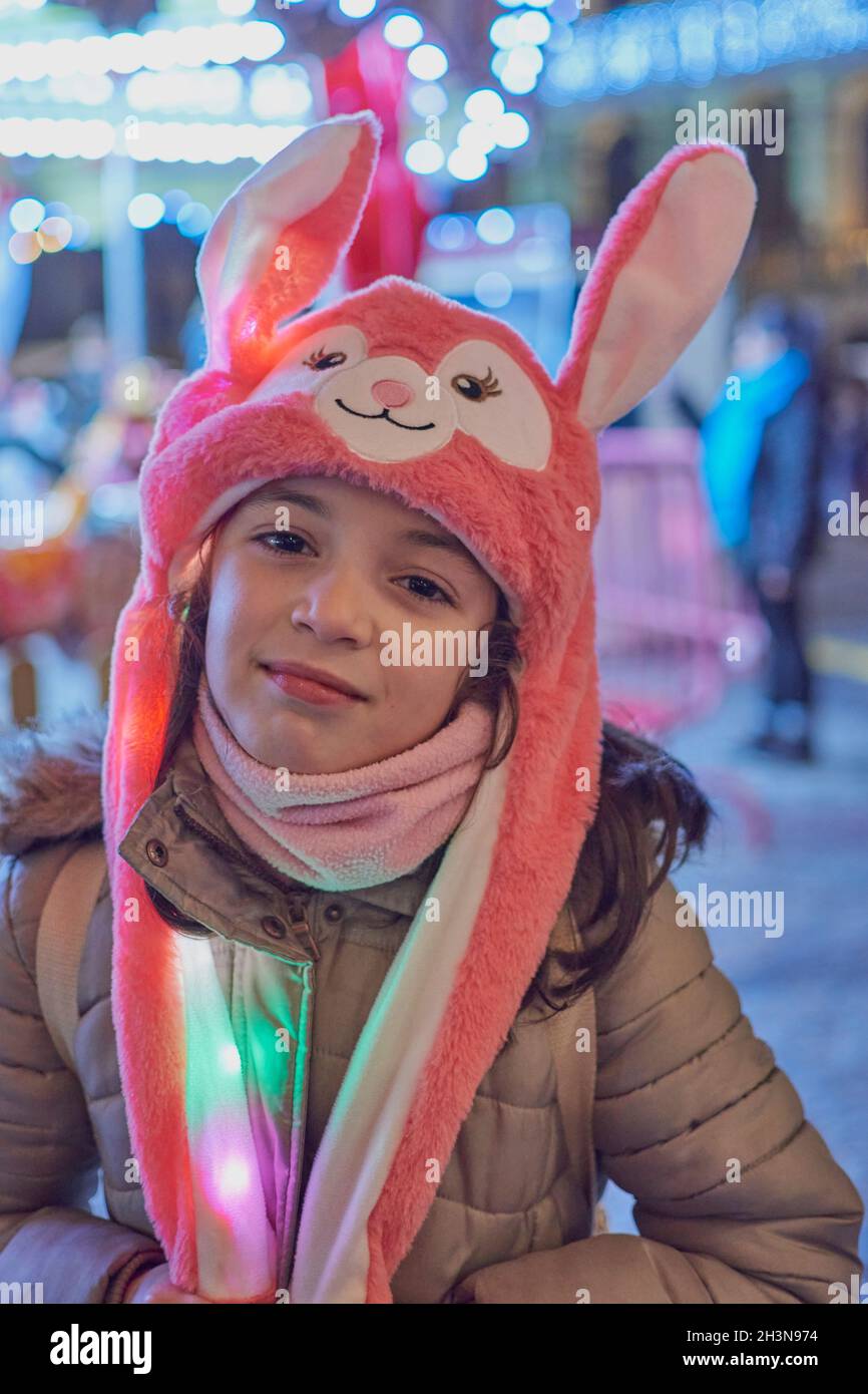 Night view of a smiling girl with a pink hat with ears lit up at Christmas in Toledo, Spain Stock Photo