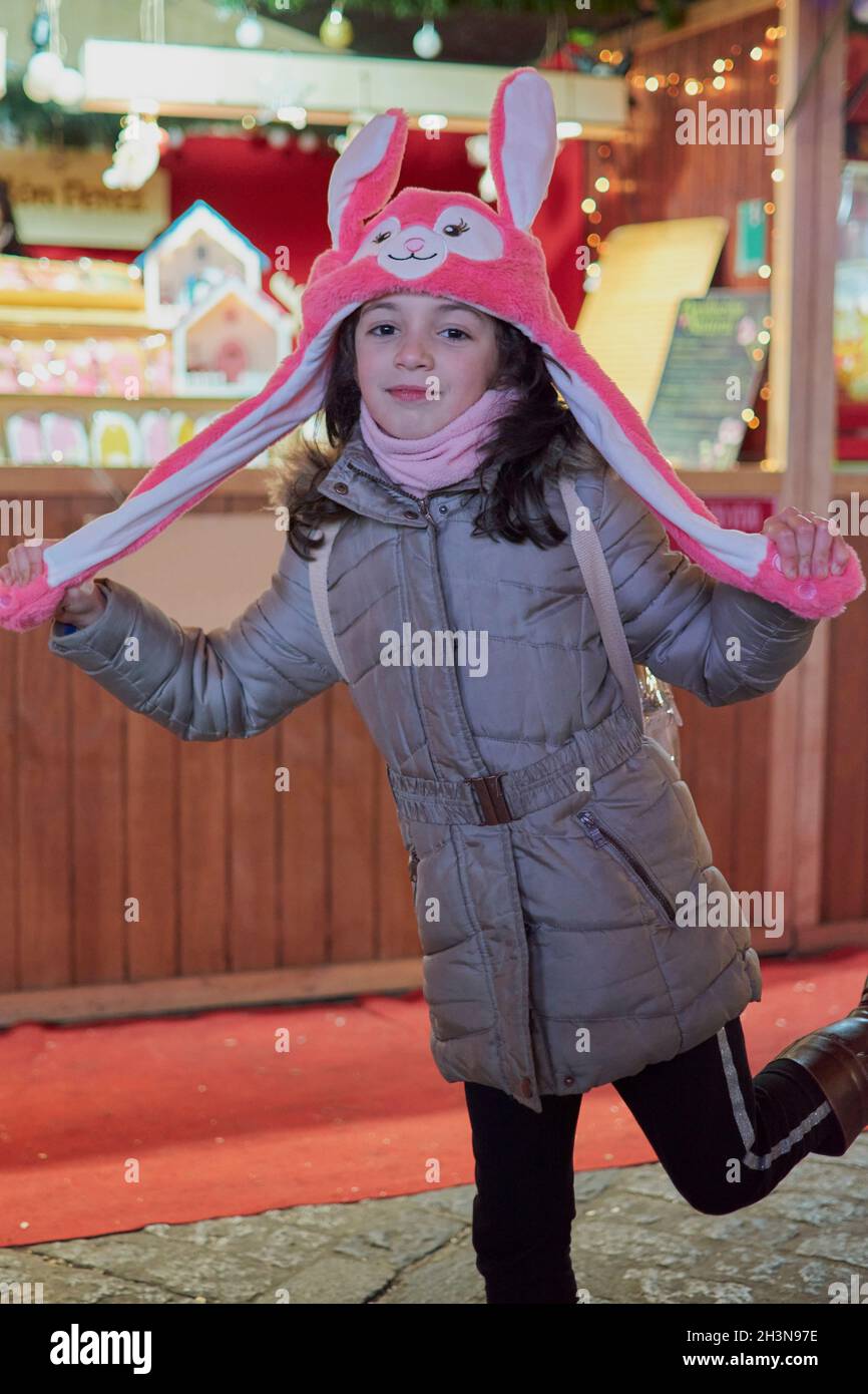 Night view of a smiling girl with a pink hat with ears lit up at Christmas in Toledo, Spain Stock Photo