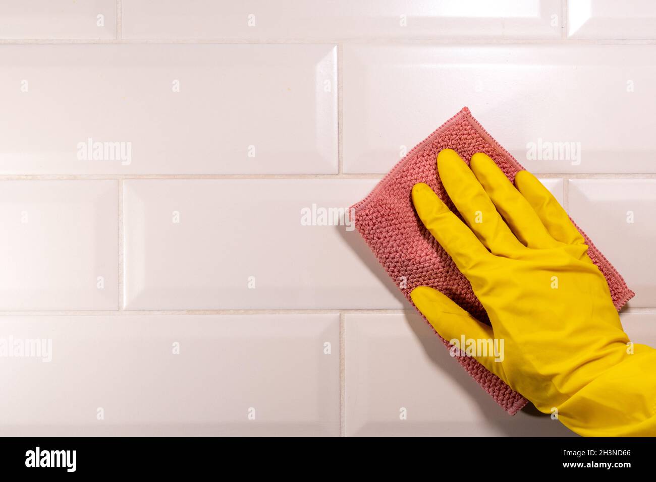 Hand in a yellow rubber glove wiping the ceramic tile surface with a ...