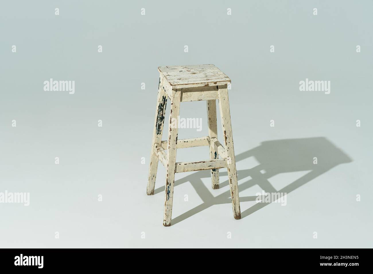Tall retro stool or tabouret with peeling white paint on white background. Empty place Stock Photo