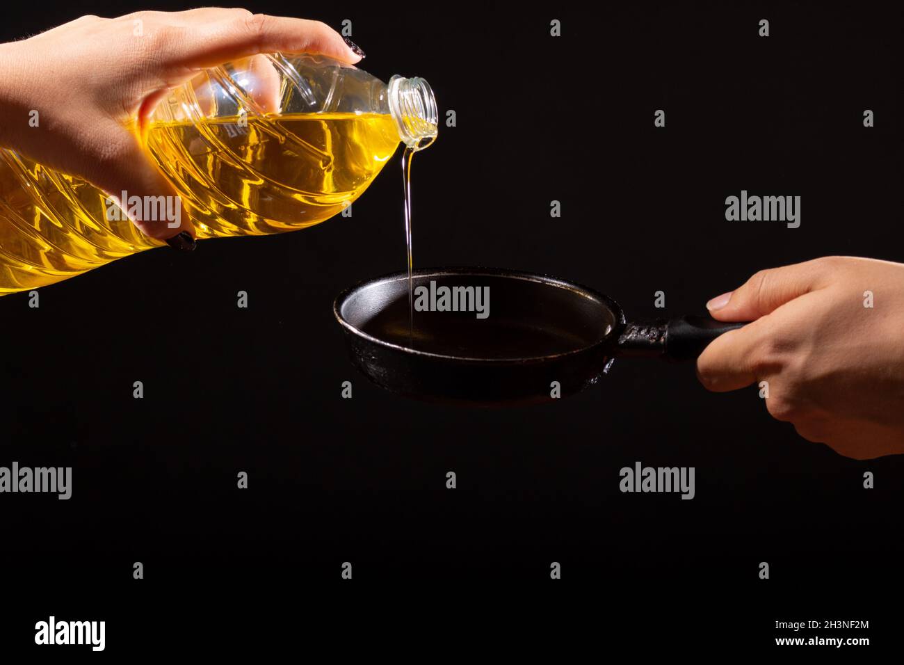 hand pouring vegetable oil on frying pan. isolated black background