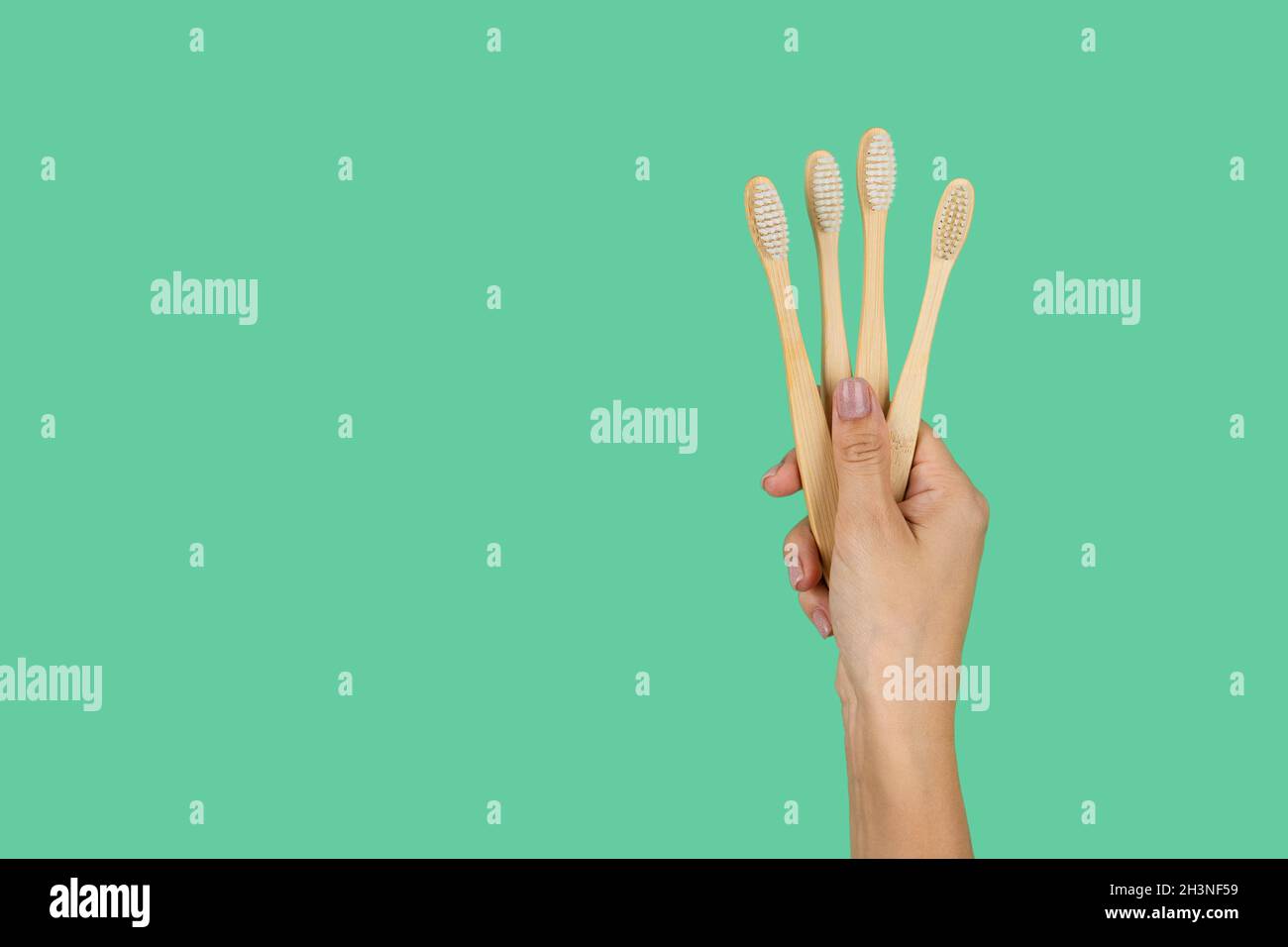 Bamboo toothbrushes in a female hand on a mint background with a place ...