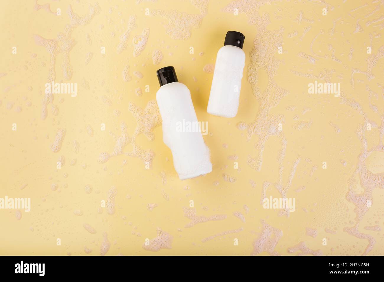 Two plastic bottles of different size on light yellow. No label. Close up, top view, copy space for text or logo. Stock Photo