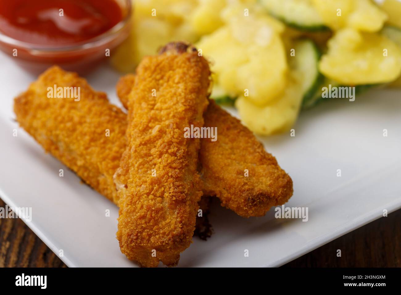 Fish fingers with potato salad on the plate Stock Photo
